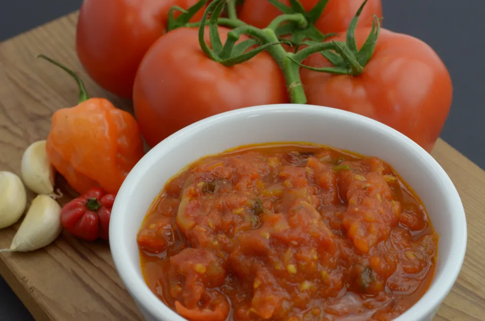 Tomato choka in a bowl and raw tomatoes, pepper and garlic on side